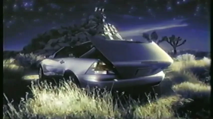 A silver convertible car with its trunk open is parked in a desert landscape at night, surrounded by tall grass and cacti under a starry sky.