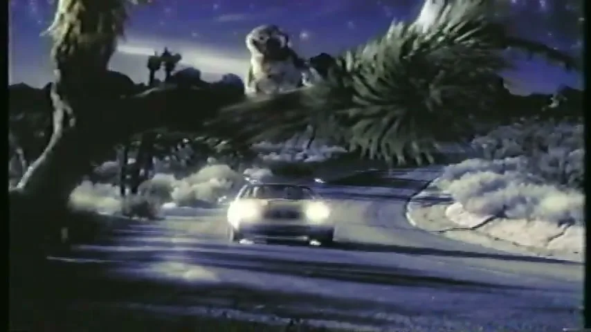 A white Mercedes-Benz drives on a winding desert road at night, with an owl perched on a tree in the foreground.
