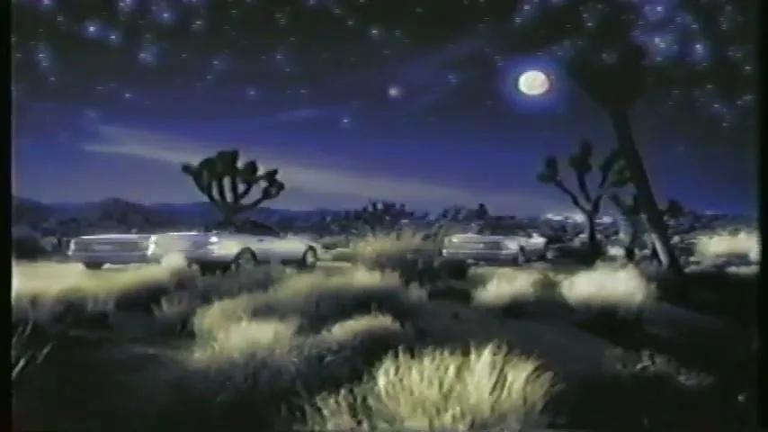 Three Mercedes-Benz cars drive through a desert landscape at night under a starry sky with a full moon.