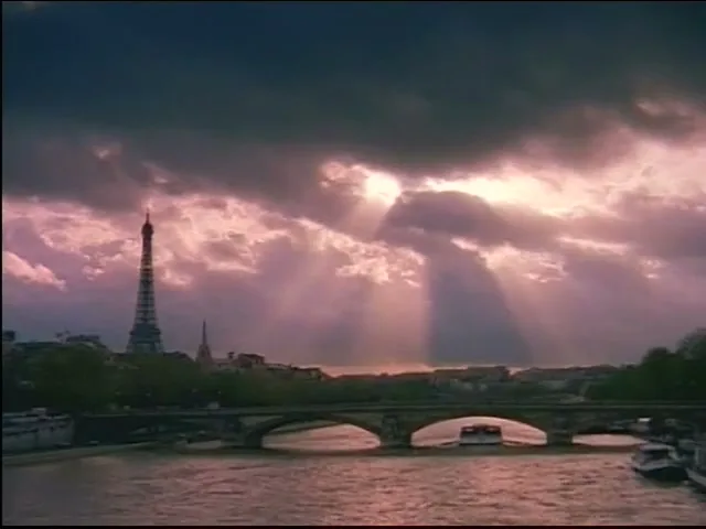 A wide shot of the Eiffel Tower and a bridge over the Seine River in Paris, with dramatic, sun-drenched clouds in the sky.