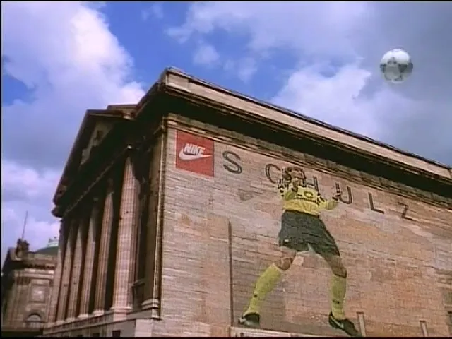 A giant soccer player mural on a brick building kicks a soccer ball into the sky, with a Nike logo visible on the wall.