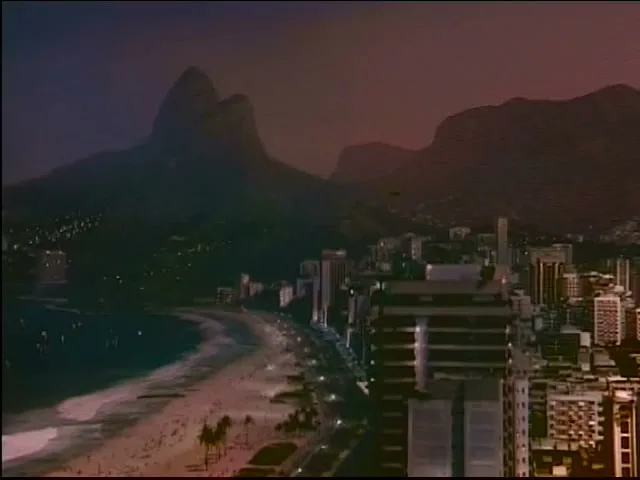 An aerial view of a city beach with mountains in the background at dusk, showing buildings along the coastline.