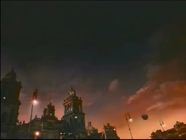 A wide shot of a dark city skyline with historic buildings and streetlights, under a dramatic sky with orange clouds at dusk.