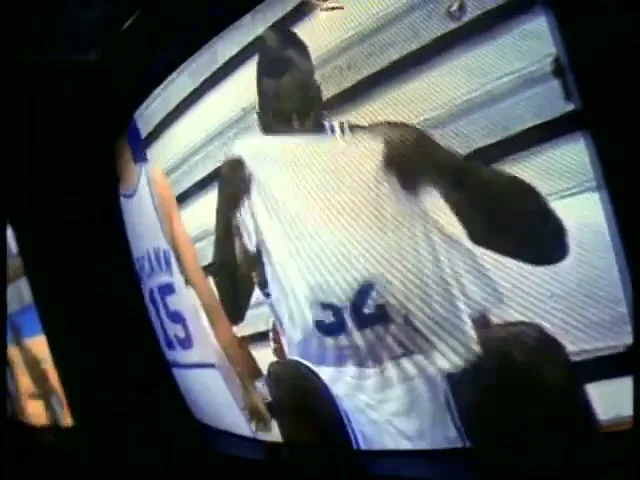 A male basketball player in a white jersey with number 32 wipes his face with a towel, seen through a distorted CRT television screen.