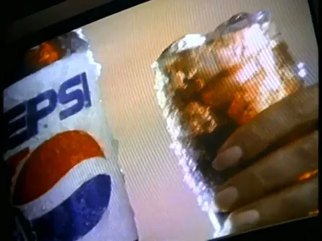 A hand holds a glass of Pepsi with ice, next to a cold Pepsi can, on a light background.