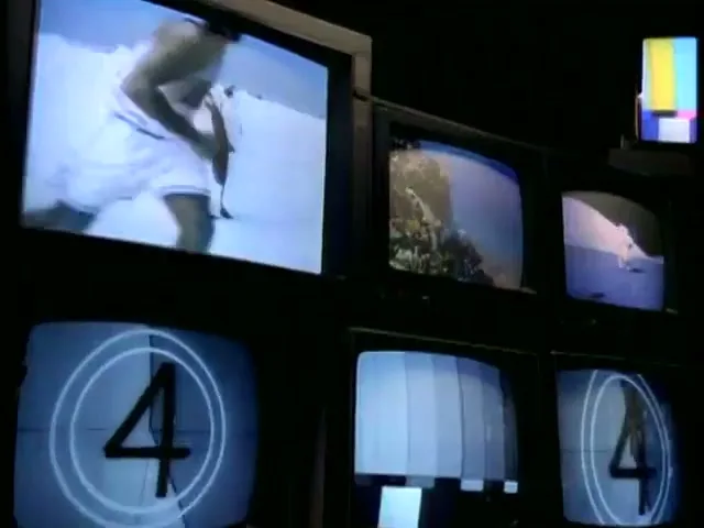 A man in a white tank top and shorts runs past penguins on a snowy landscape, displayed on a TV screen among other screens showing various images and countdowns.