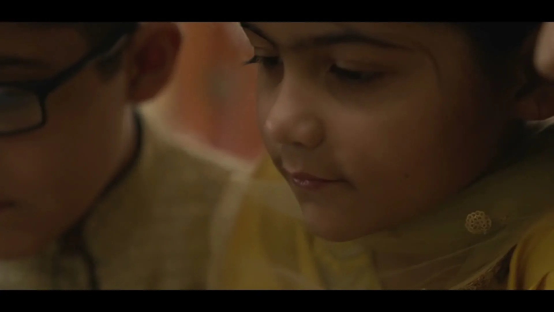 Two children, a boy and a girl, are seen in a medium closeup, looking down with serious expressions in an interior setting.