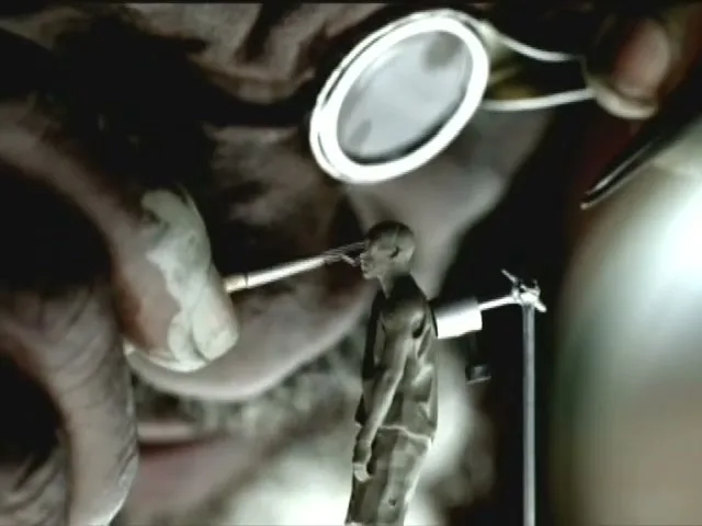 A tiny, grey, male figurine is being worked on by a dentist's tools, with a dental mirror above, in a dark, mysterious setting.
