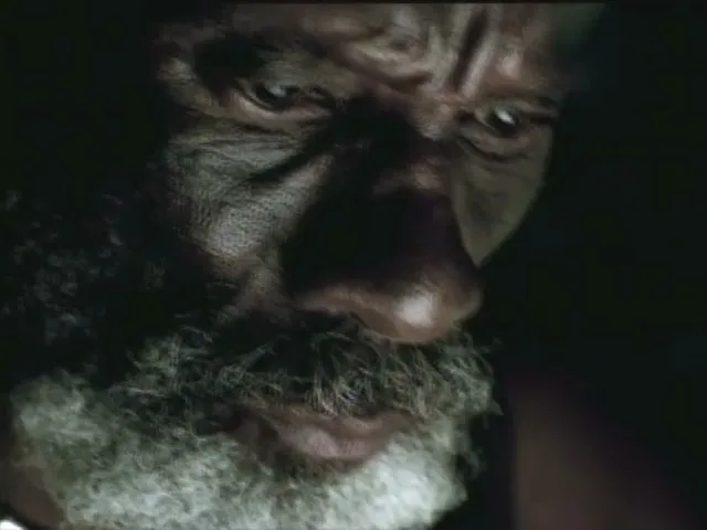 A close-up shot shows a man's face with a grey beard, looking down intently, as if in deep thought or concentration.