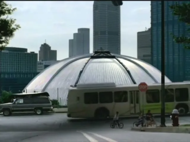 A giant hand descends from the sky over a city street with a bus, cars, and children on bikes, with a large domed building and skyscrapers in the background.