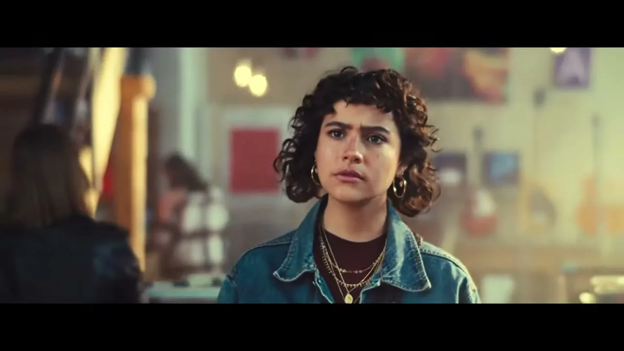 A young woman with curly hair and a denim jacket looks concerned in a music store.