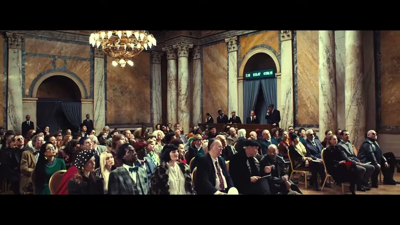 A diverse group of people, dressed in formal and semi-formal attire, sit in an ornate auction hall, looking towards the front where an auctioneer stands.