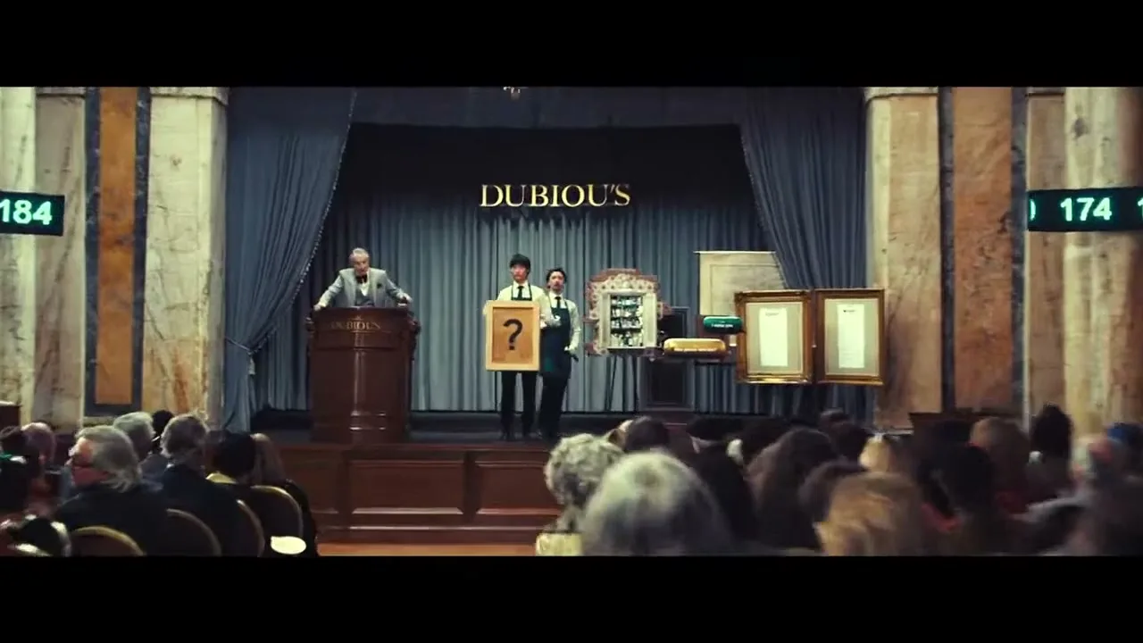 An auctioneer stands at a podium, while two assistants present items, including a framed question mark, to a seated audience in a grand auction hall.
