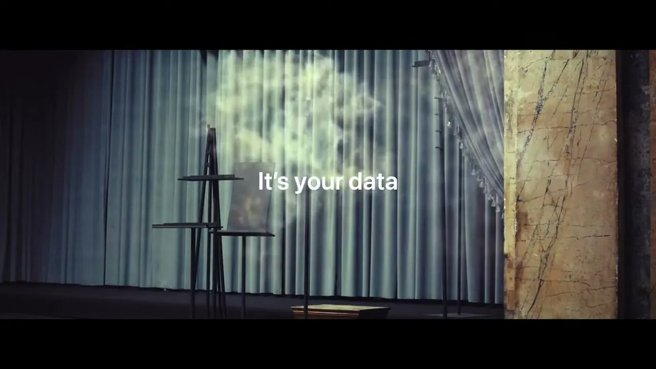 Two framed screens displaying email inboxes are shattered by a cloud of smoke, revealing the text "It's your data" on a stage with blue curtains.
