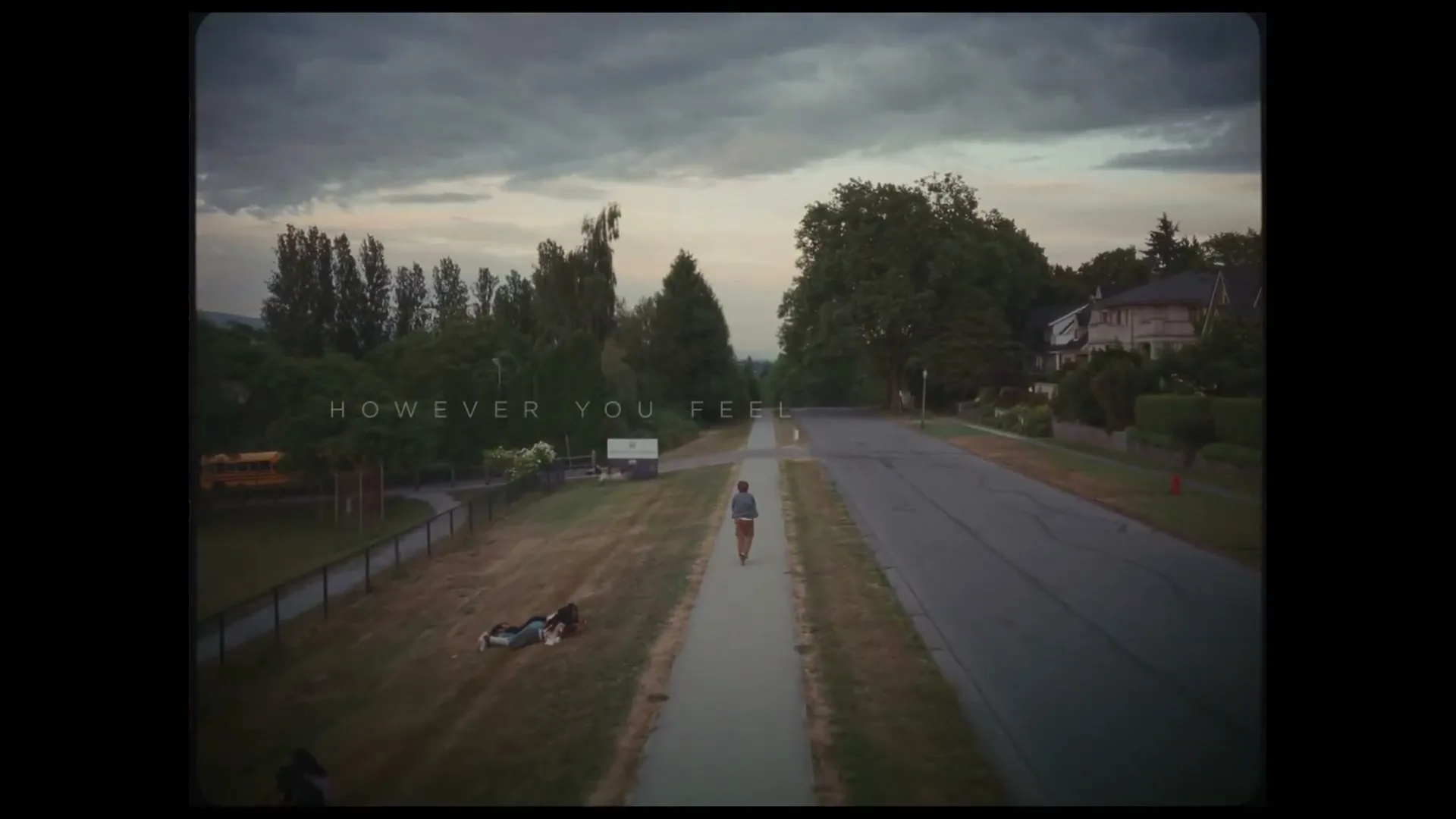 A young man walks down a sidewalk in a suburban neighborhood at dusk, with text appearing on screen.