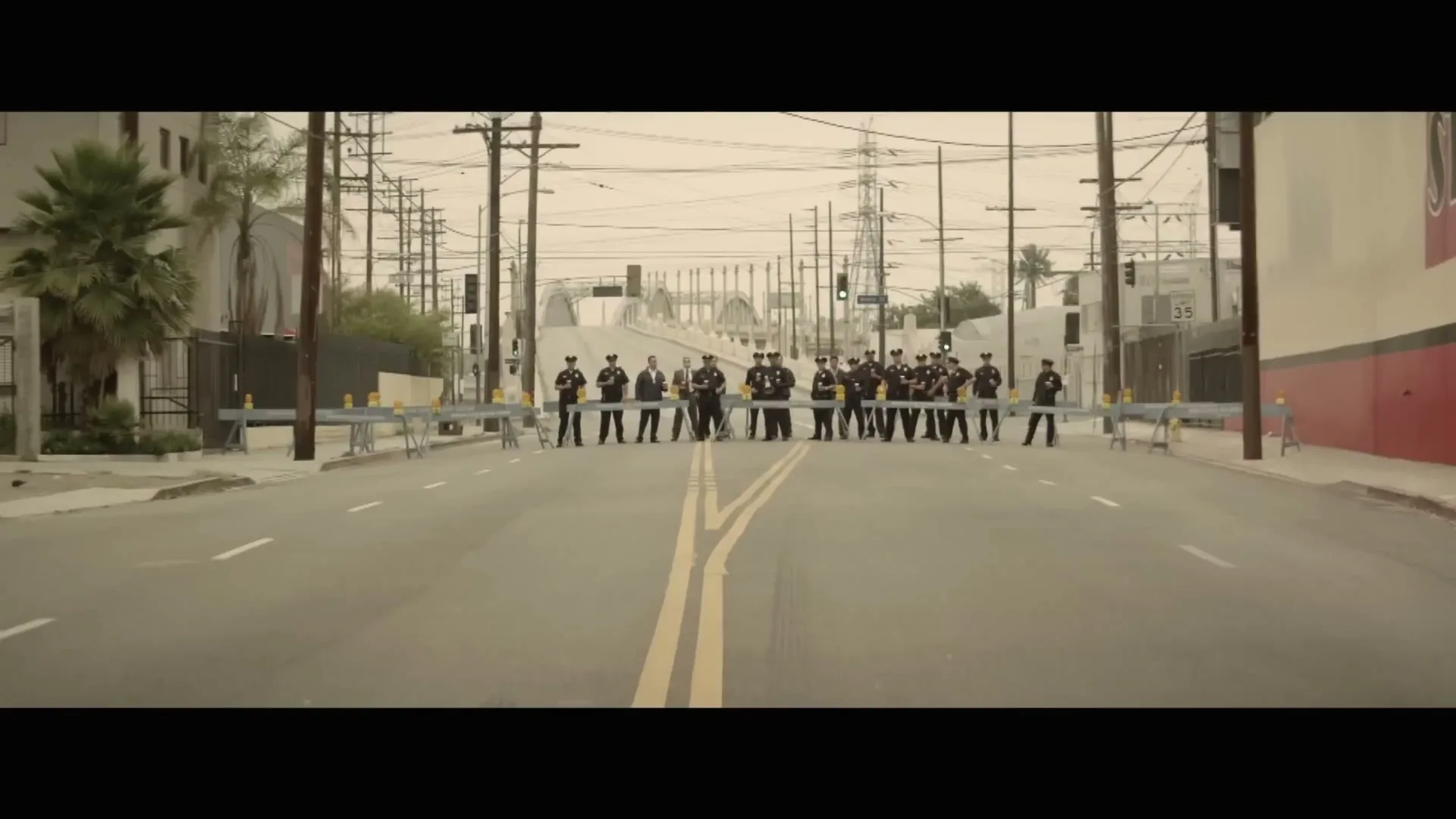 A group of police officers in uniform stand in a line across a deserted street, forming a blockade in an urban area.