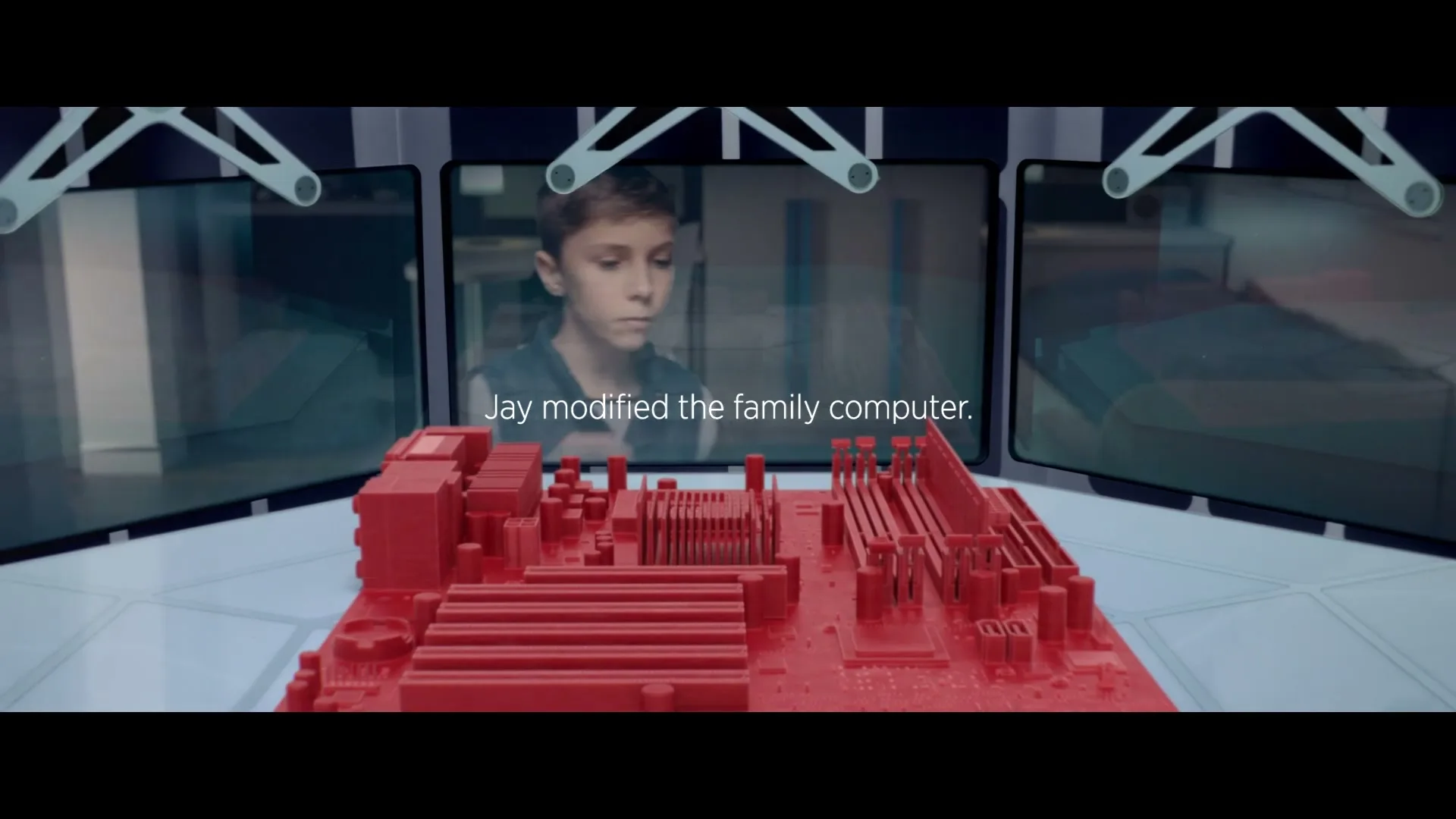 A young boy is seen through three screens, working on a red 3D-printed computer motherboard on a futuristic white table.