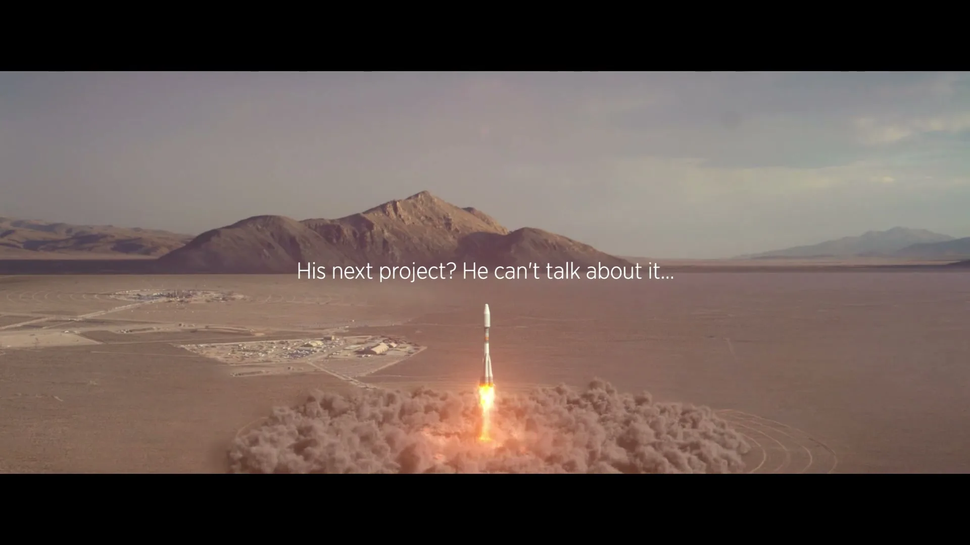 A rocket launches from a desert landscape, with mountains in the background and a small settlement visible in the distance, under a cloudy sky.