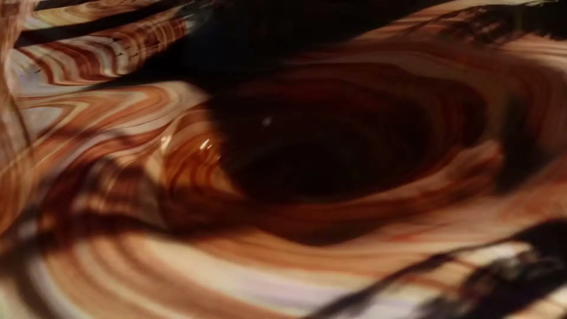 The camera moves through a dark, swirling vortex of brown and orange liquid, eventually revealing a wide shot of a desert landscape with towering rock formations under a clear sky.