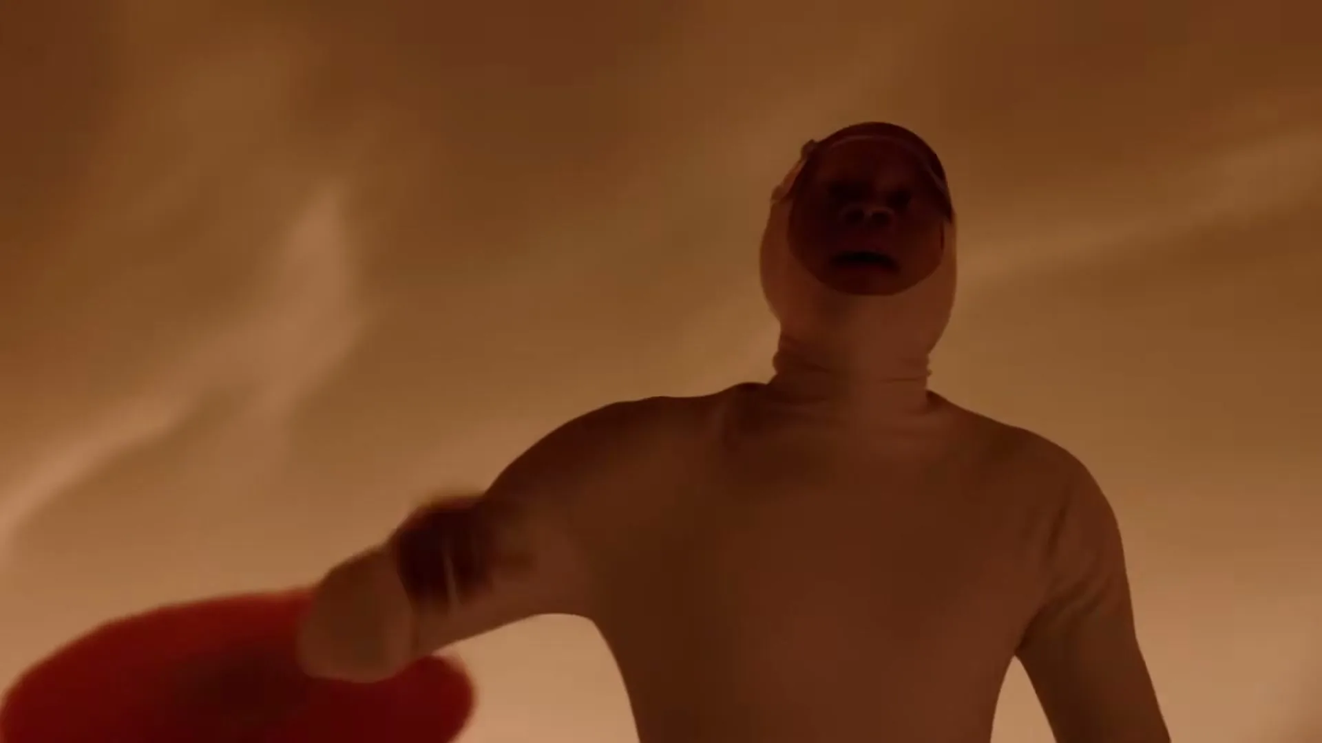 A person in a white full-body suit with their face exposed looks up in awe, raising their hand in a vast, orange-hued, otherworldly landscape.