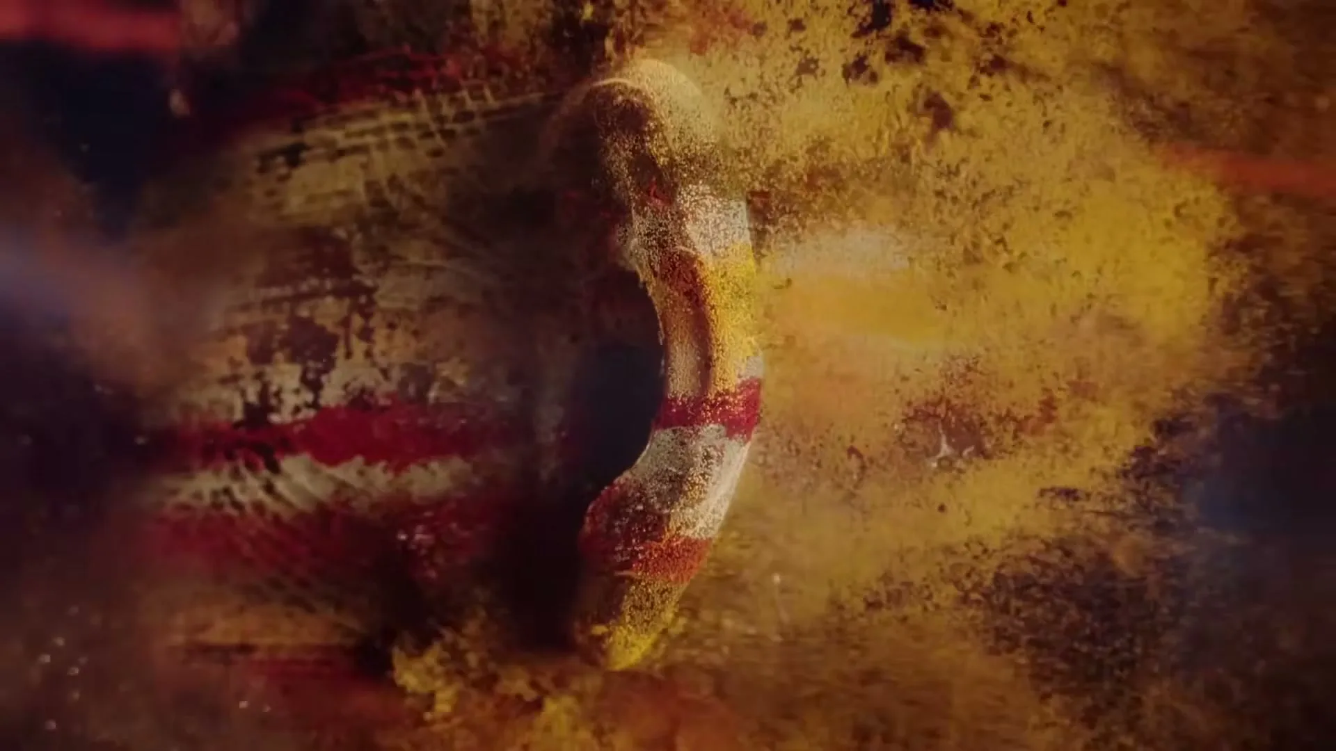 A close-up shot of a human ear, covered in red and yellow powder, as the powder slowly disperses into the air.
