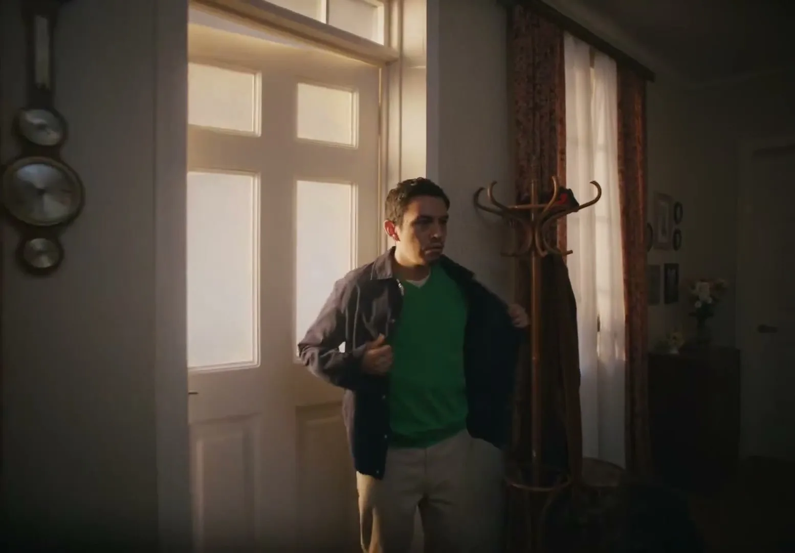 A man enters a dimly lit house through a bright doorway, taking off his jacket as a dog watches him in the foreground.