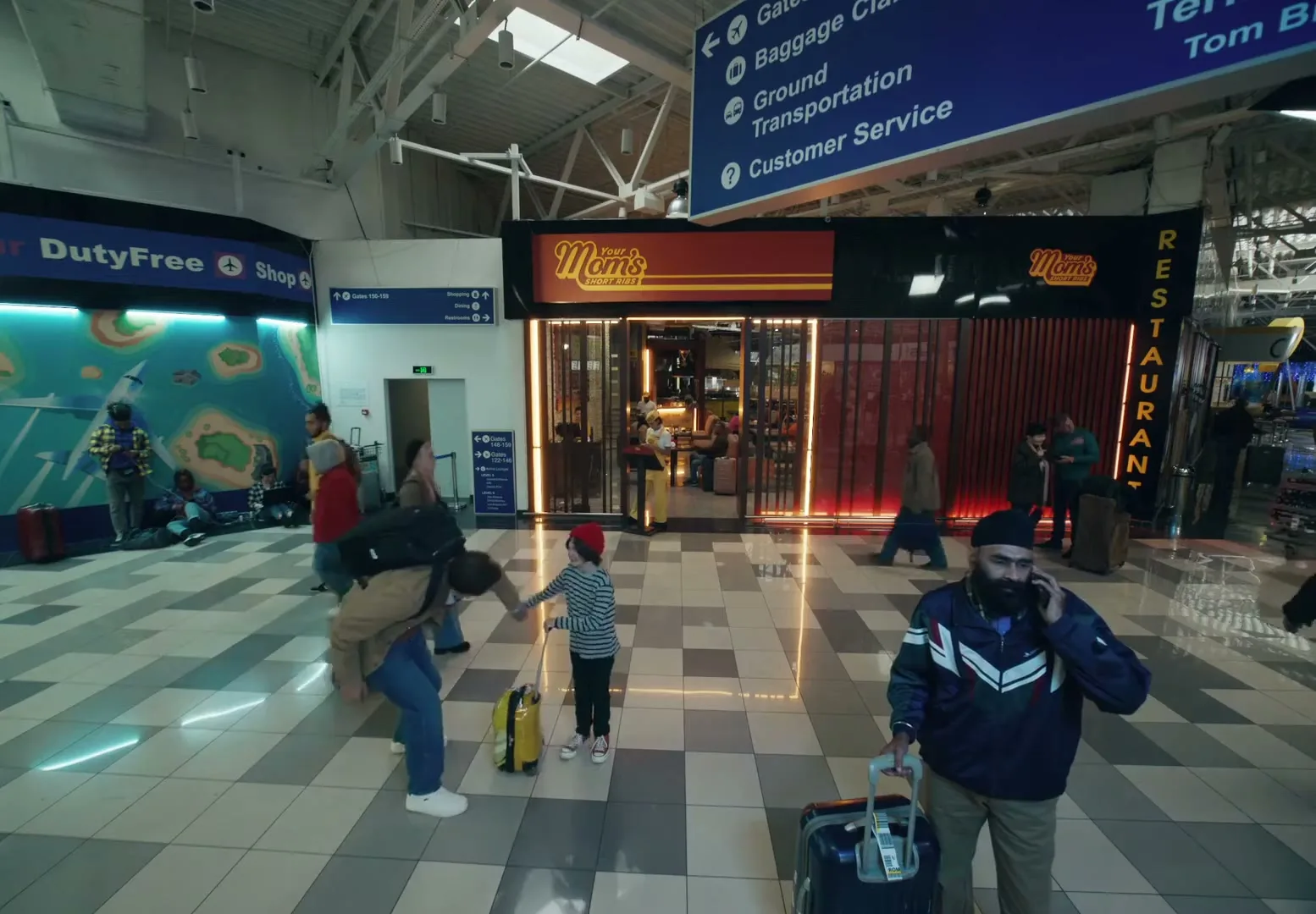 A diverse group of travelers walk through a busy airport terminal, passing by a restaurant called "Mom's" with a bright red sign.