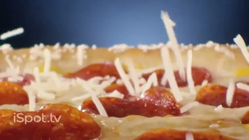Shredded cheese falls onto a pepperoni pizza with a stuffed crust, against a dark blue background.