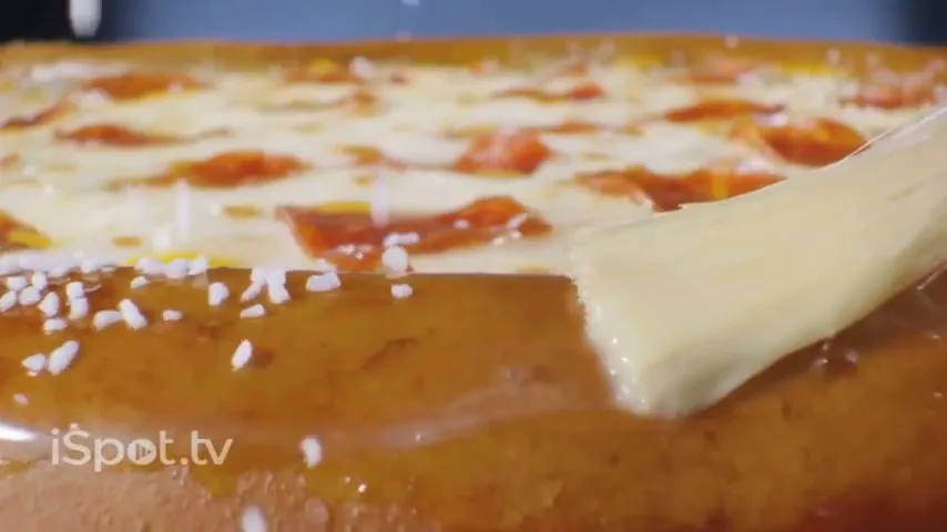 A close-up shot shows a pizza with pepperoni and cheese, as a brush applies butter to the pretzel crust and salt sprinkles down.