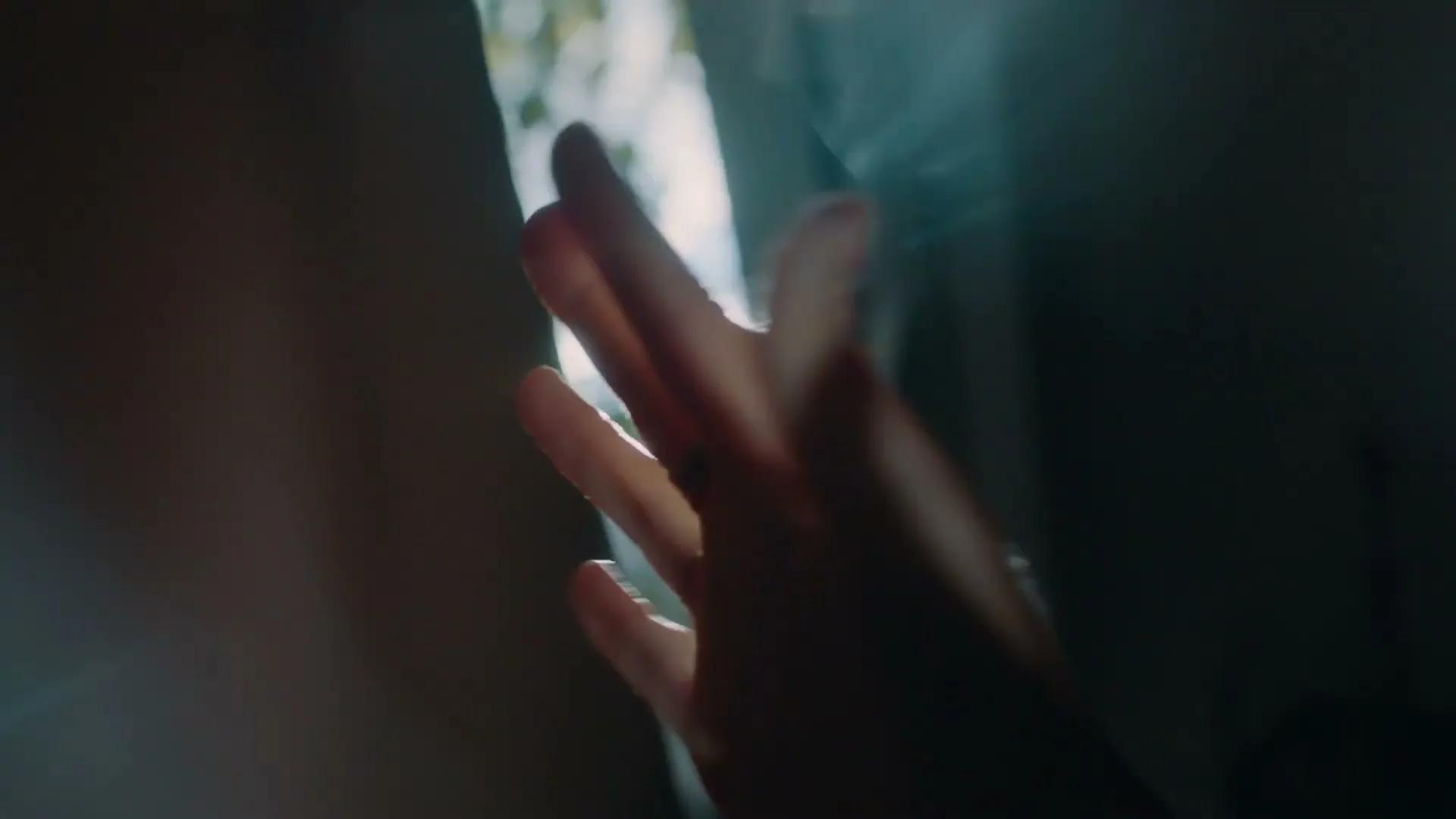 A person's hand reaches out towards a bright sunbeam shining through a window, creating a lens flare effect.