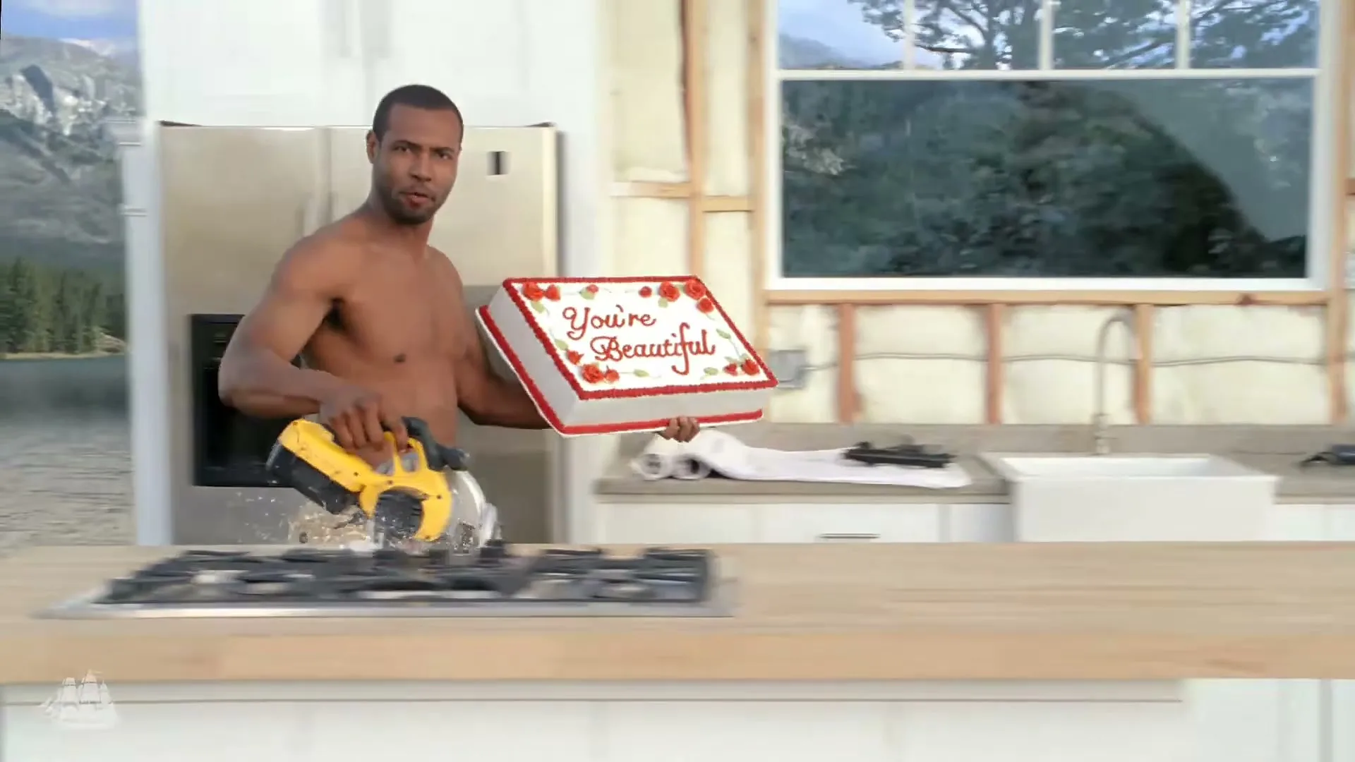 A shirtless man in khaki shorts stands in a kitchen, holding a cake that says "You're Beautiful" and a circular saw, with a lake and mountains in the background.