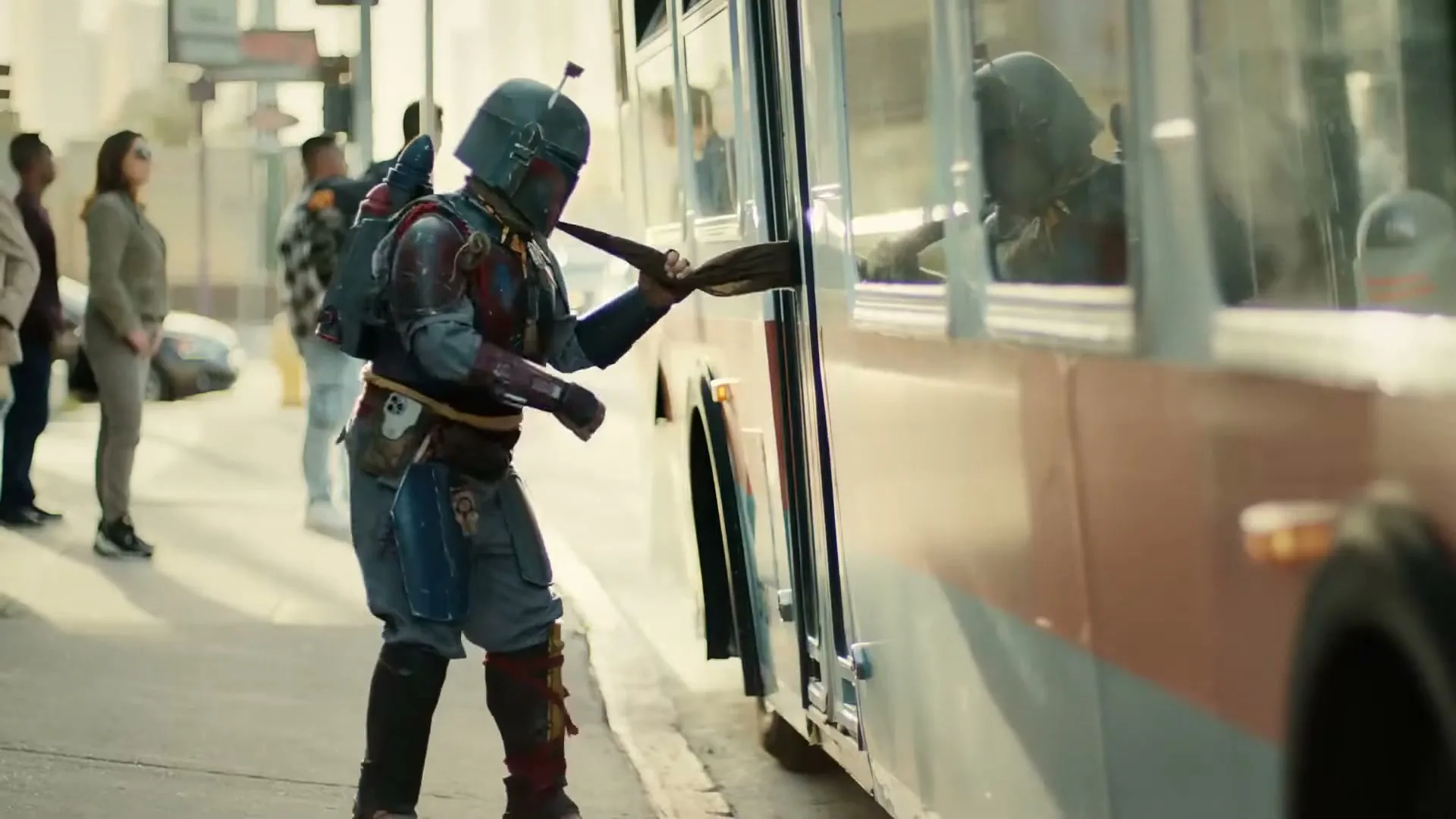 A person dressed as Boba Fett from Star Wars tries to board a bus, but the door closes on their cape, leaving them stuck on the sidewalk.