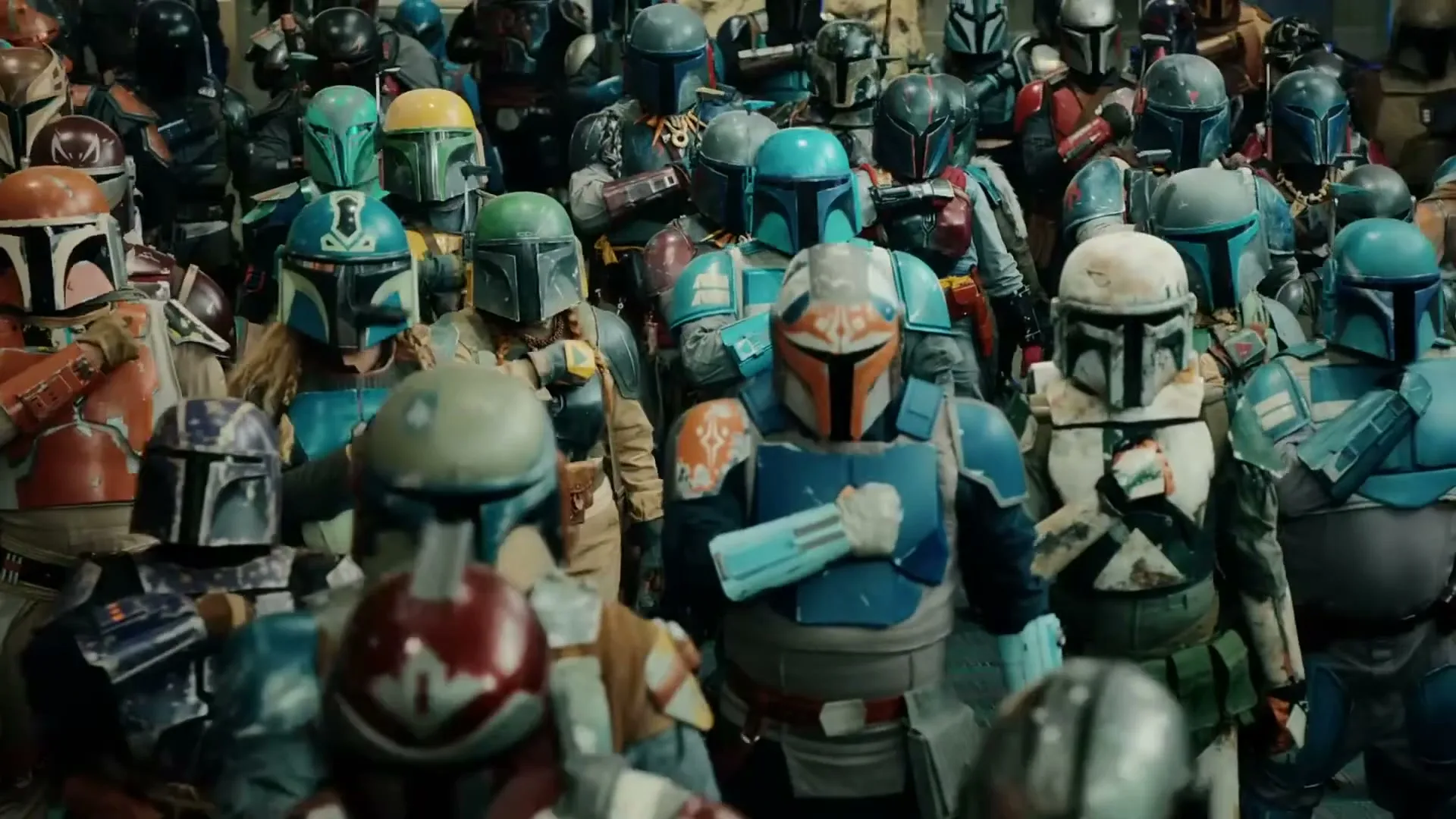 A large group of people dressed in colorful Mandalorian armor and helmets stand together in a crowded indoor space.