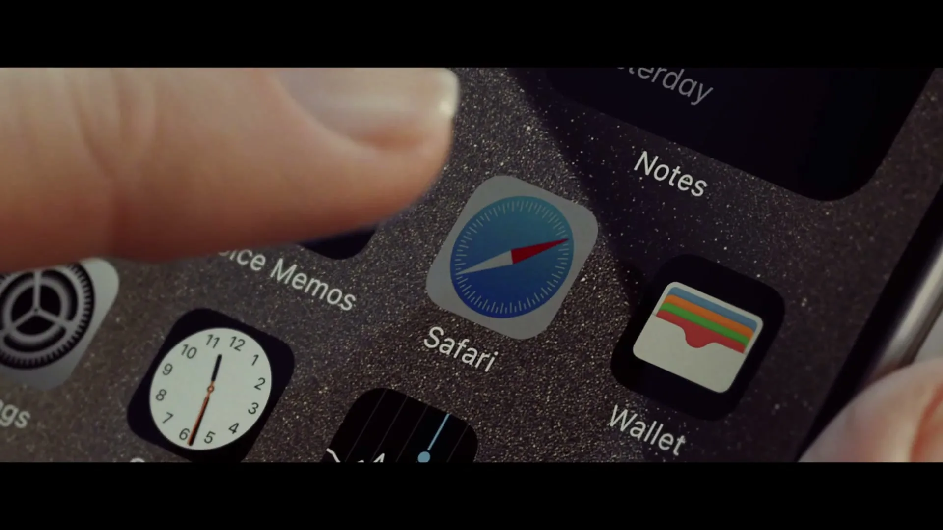A finger taps the Safari app icon on a dusty iPhone screen, surrounded by other app icons like Notes and Wallet.
