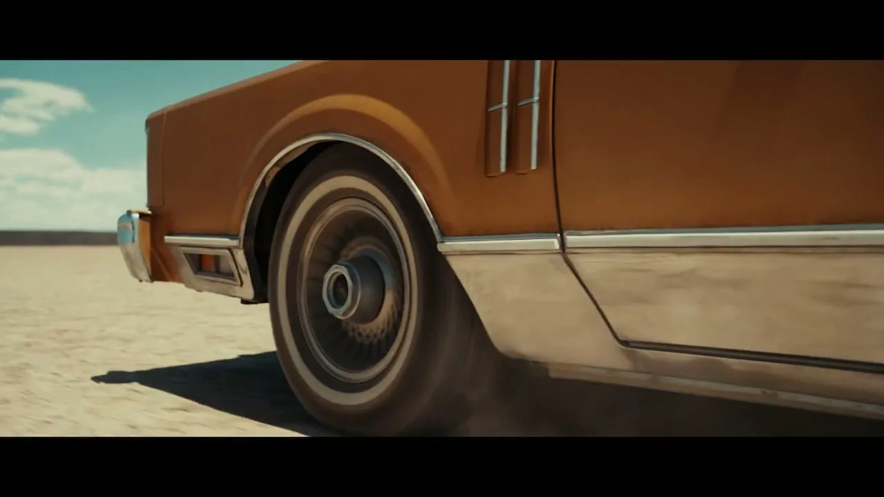 A close-up shot of a vintage brown car's rear wheel spinning on a dusty desert road under a bright sky.