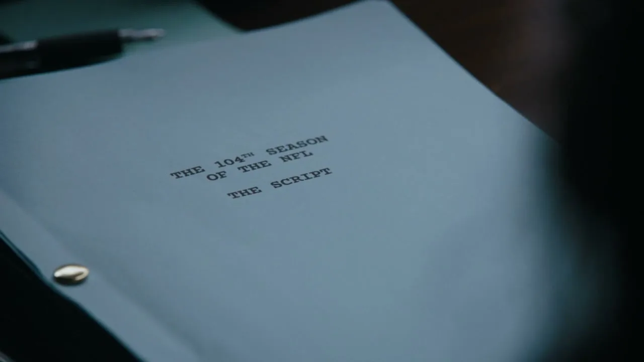 A close-up shot of a blue script cover with the title "THE 104TH SEASON OF THE NFL THE SCRIPT" on a table with a pen and notepad.