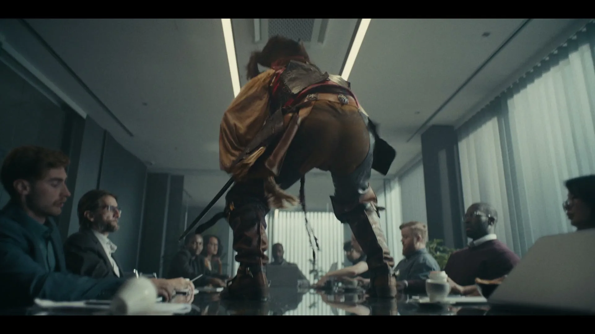 A pirate in a brown and yellow costume stands on a conference table, bending over, while business people sit around the table looking at the pirate.