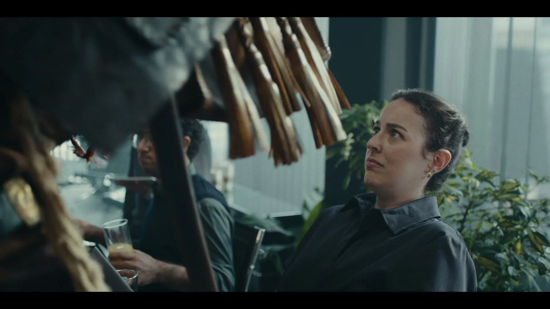 A woman in a dark shirt looks up with a concerned expression as a pirate's hat with tassels swings in front of her at an office party.