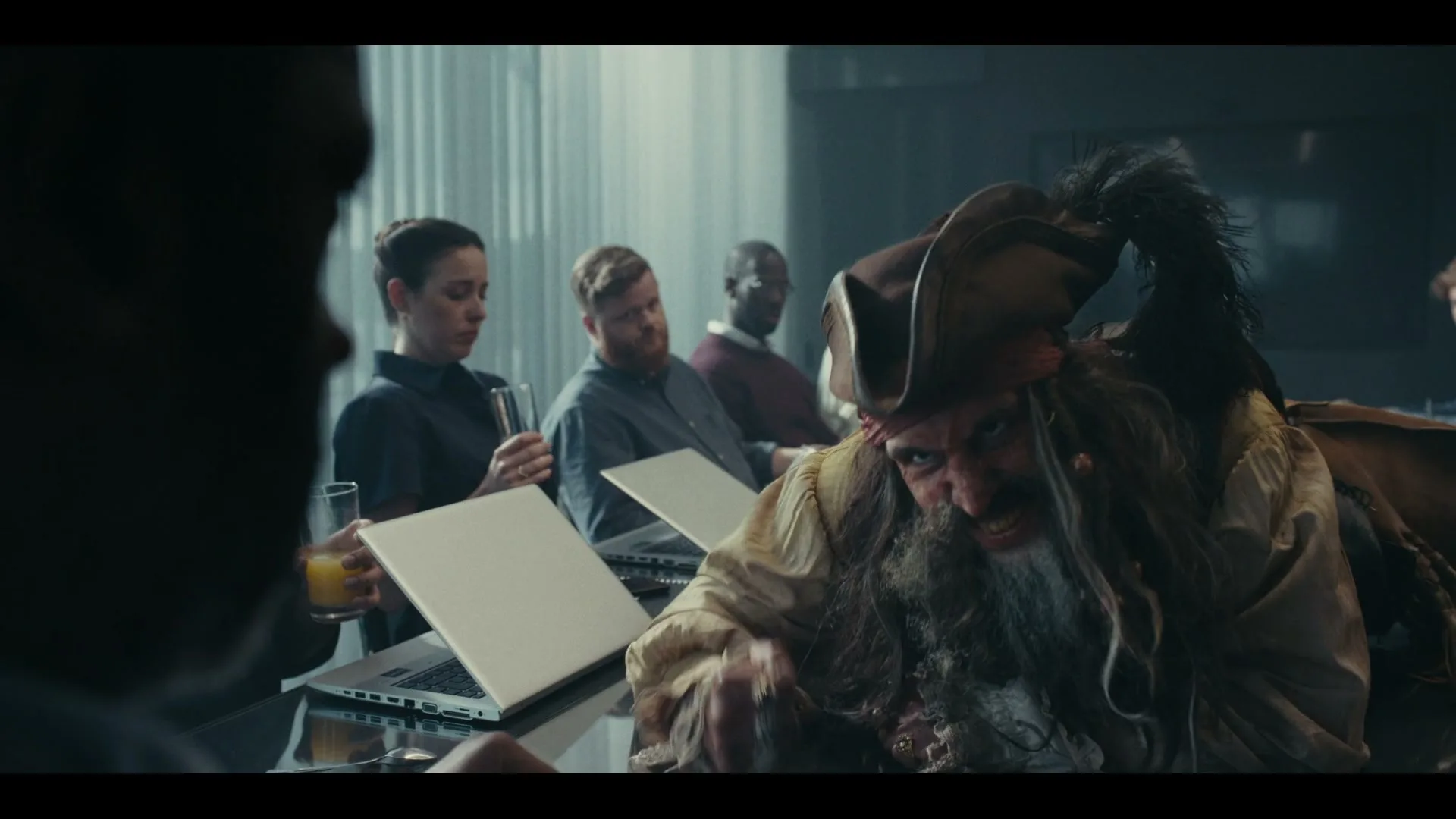 A pirate in a brown hat and long beard leans forward, snarling at an unseen person across a conference table in a modern office.