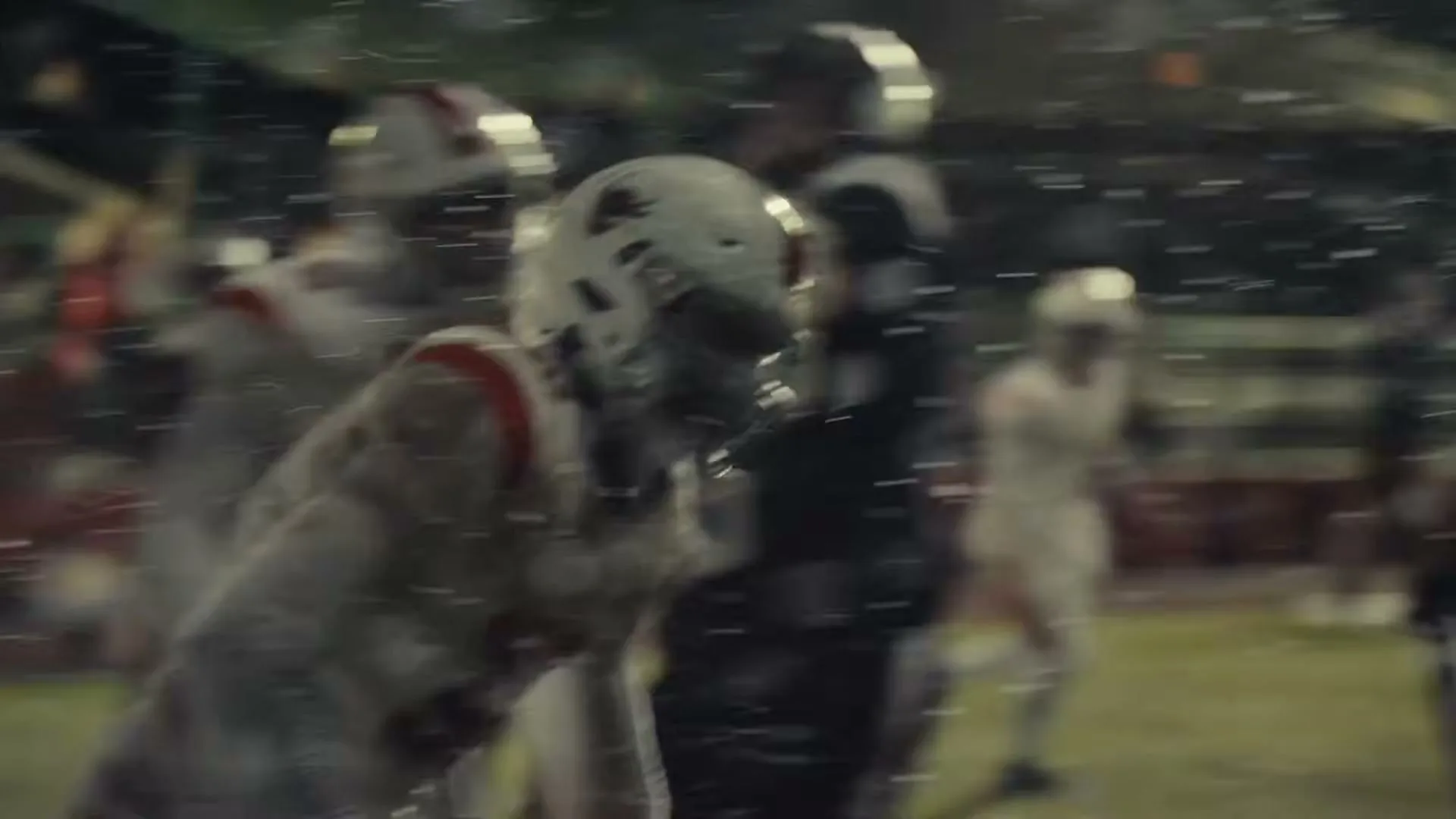 A football player in a white uniform and helmet runs on a field at night, with other players in the background.