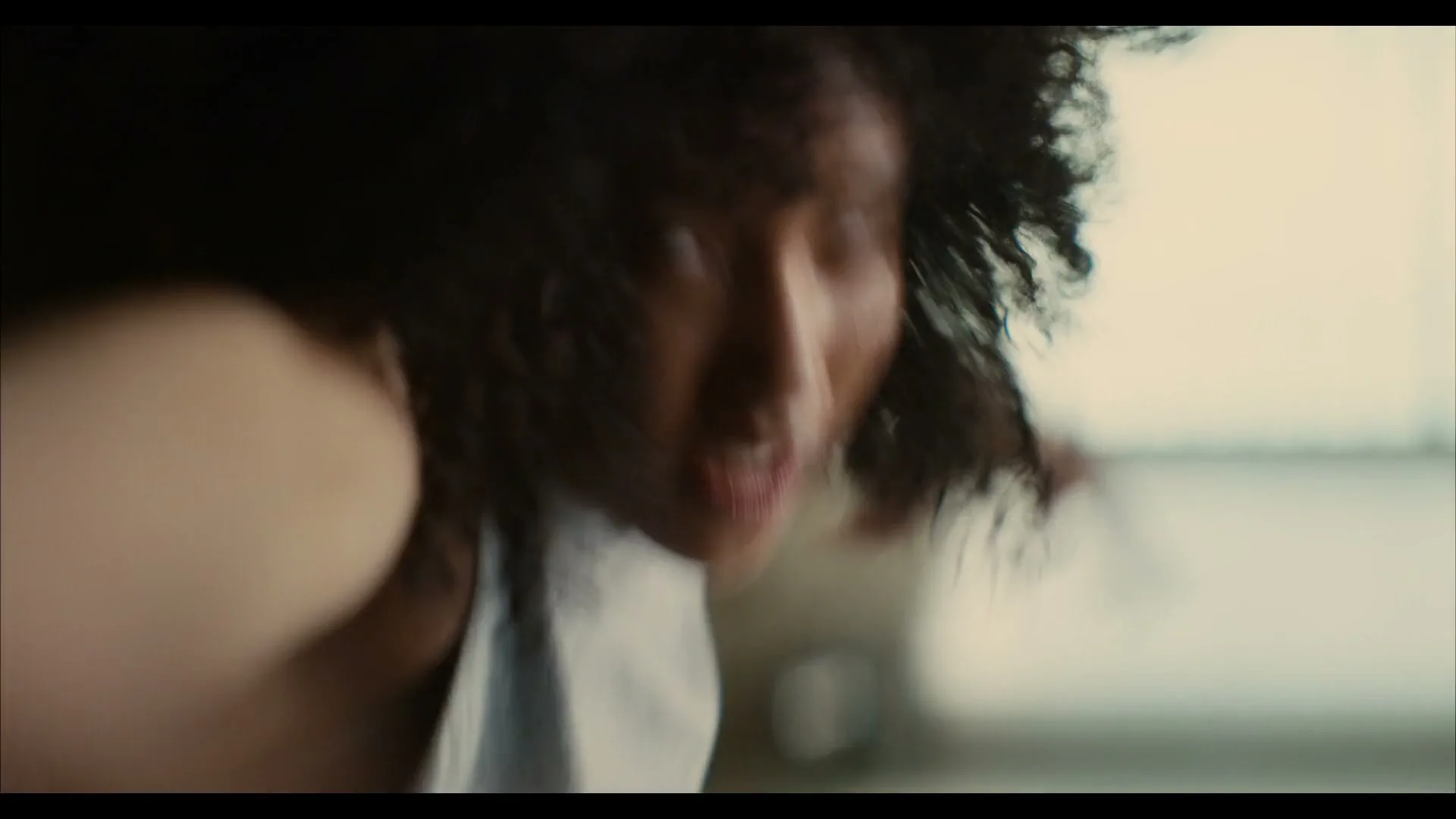 A young woman with curly hair, wearing a grey tank top, is seen in a blurry, dynamic shot, possibly exercising indoors.