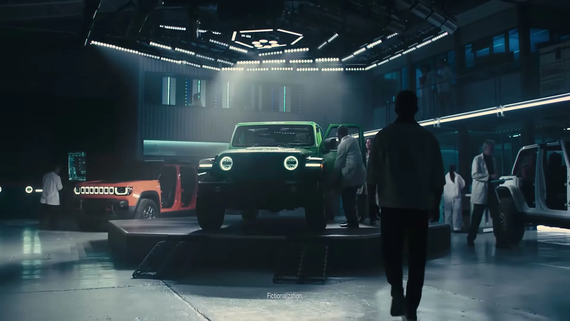 A man in a dark jacket walks towards a green Jeep Wrangler on a rotating platform in a futuristic lab, while scientists in lab coats work around other Jeeps.