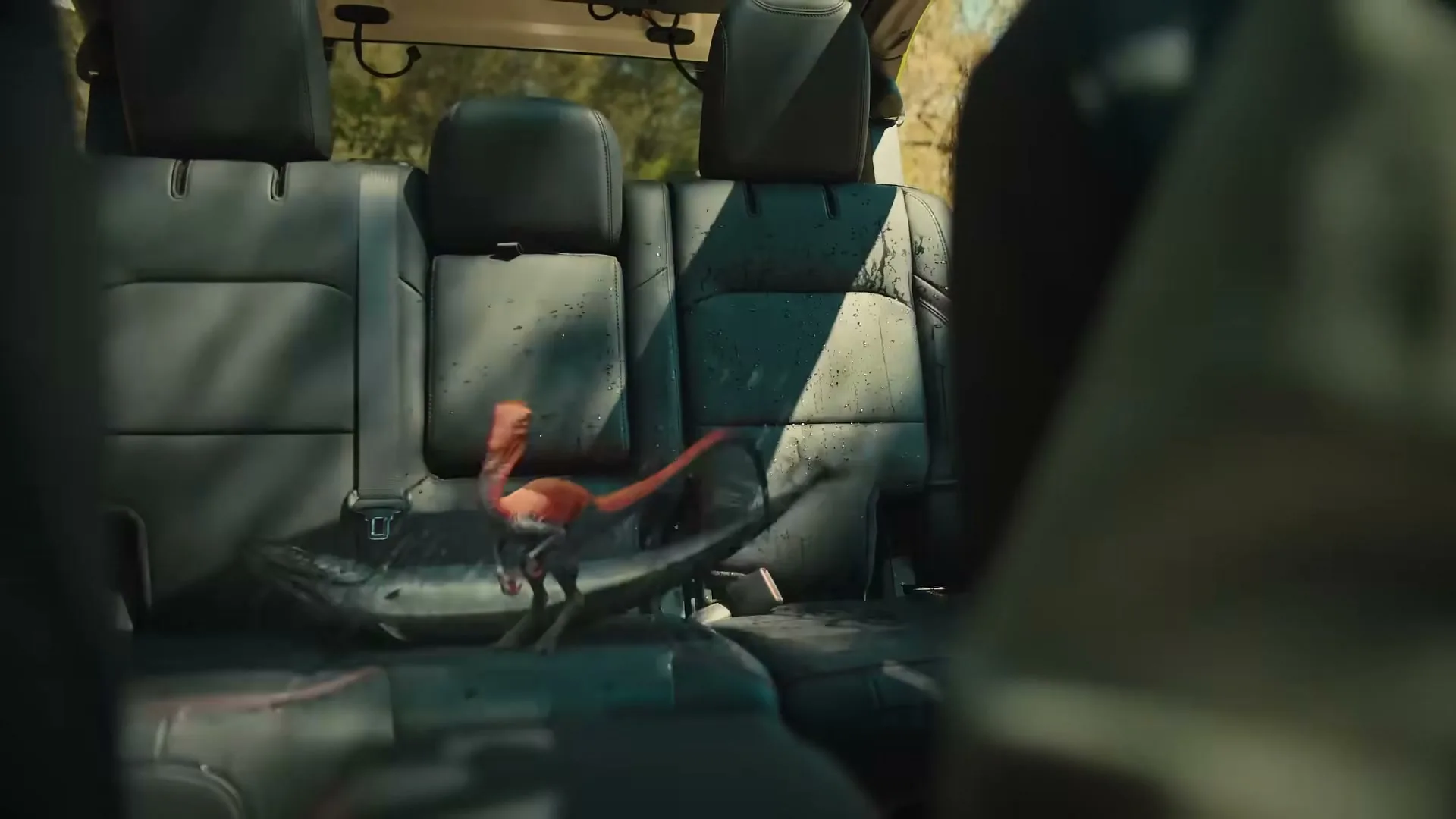 A small, red dinosaur-like creature with a long tail jumps around on the back seats of a car, with water splashing around it.