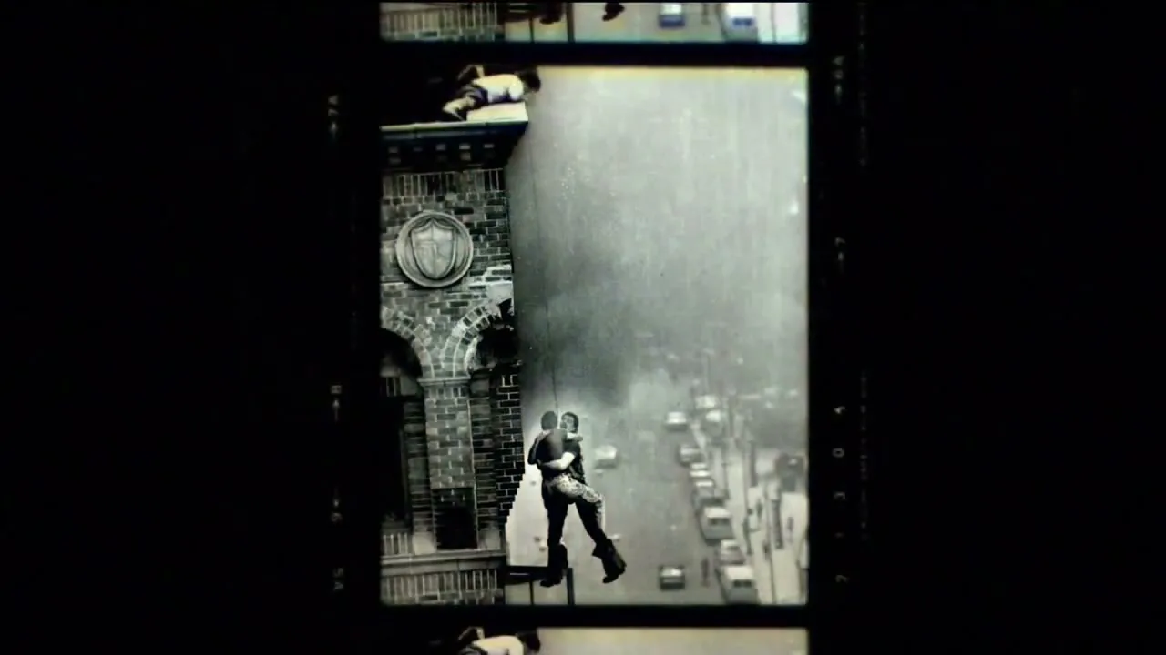 A black and white archival footage shows a man hanging from a building, with a street and cars visible below, framed within a film strip.