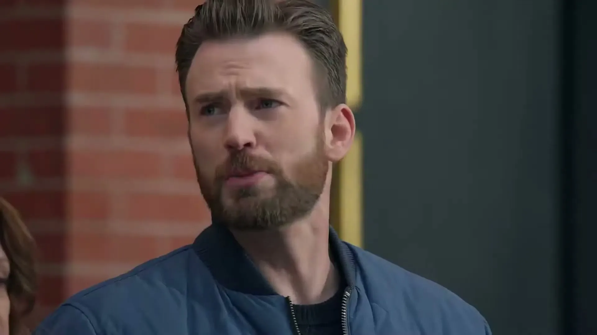 A man with a beard and blue jacket looks around with a surprised expression on a city street.