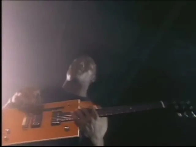 Bo Jackson, a male in his 20s, plays an orange electric guitar in a dark, smoky studio.
