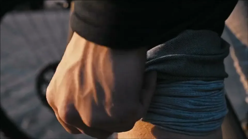 A person's hand rolls up the cuff of their denim jeans, revealing their leg, with a bicycle wheel blurred in the background.