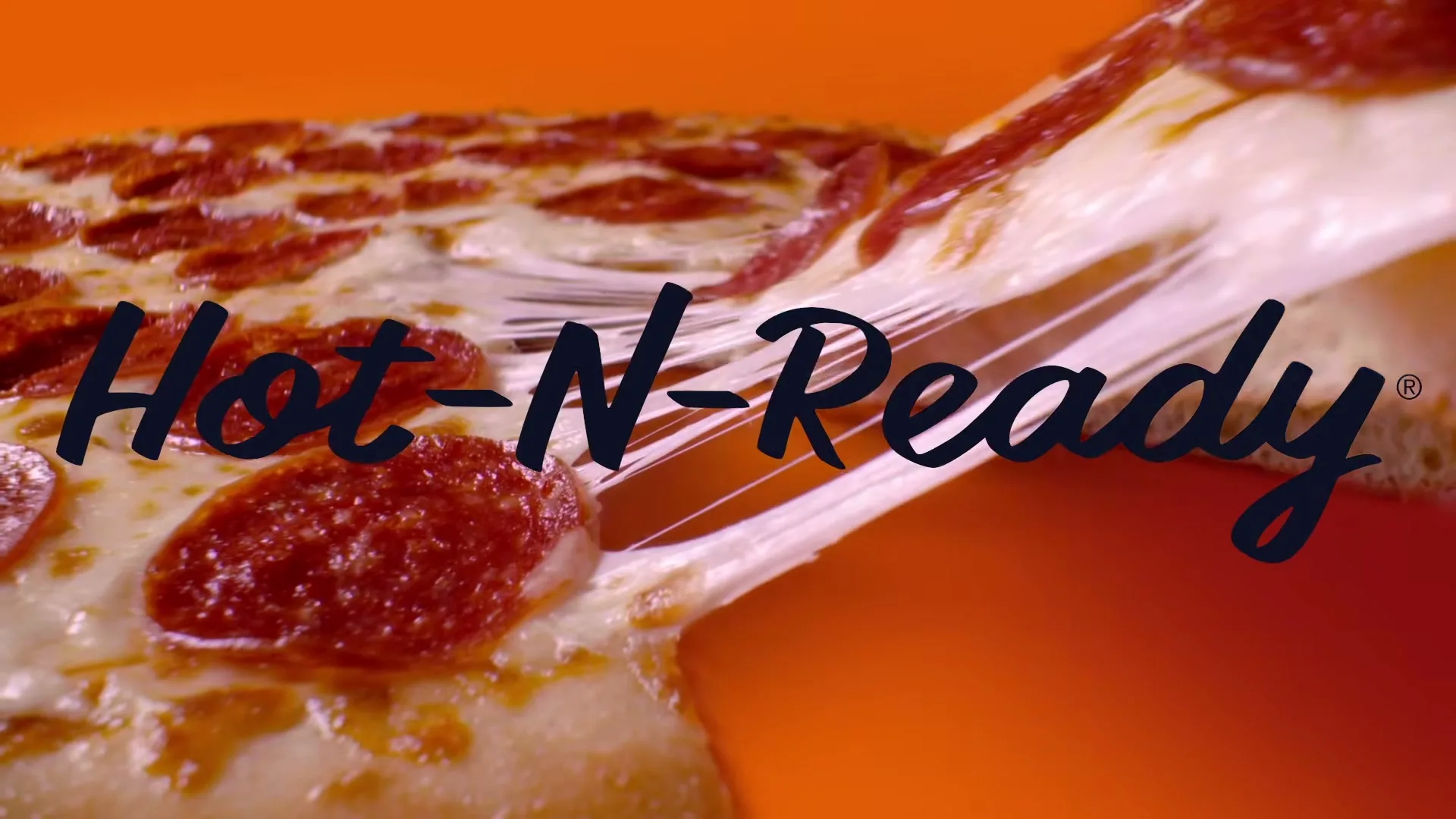 A slice of pepperoni pizza is pulled from a whole pizza, creating long, stretchy cheese strings against an orange background.