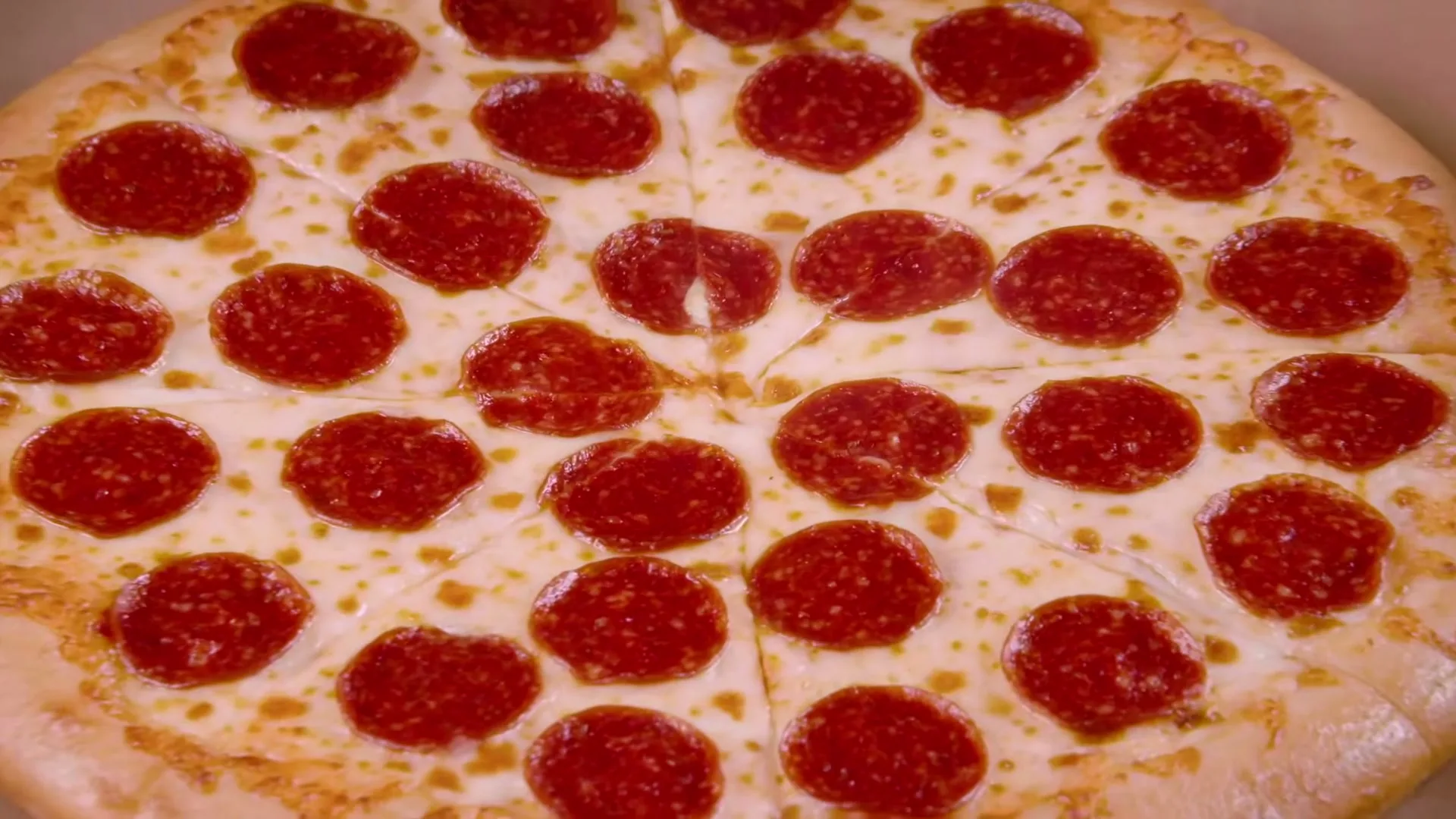 A freshly baked pepperoni pizza, sliced into wedges, is shown in a close-up shot, still inside its cardboard box.
