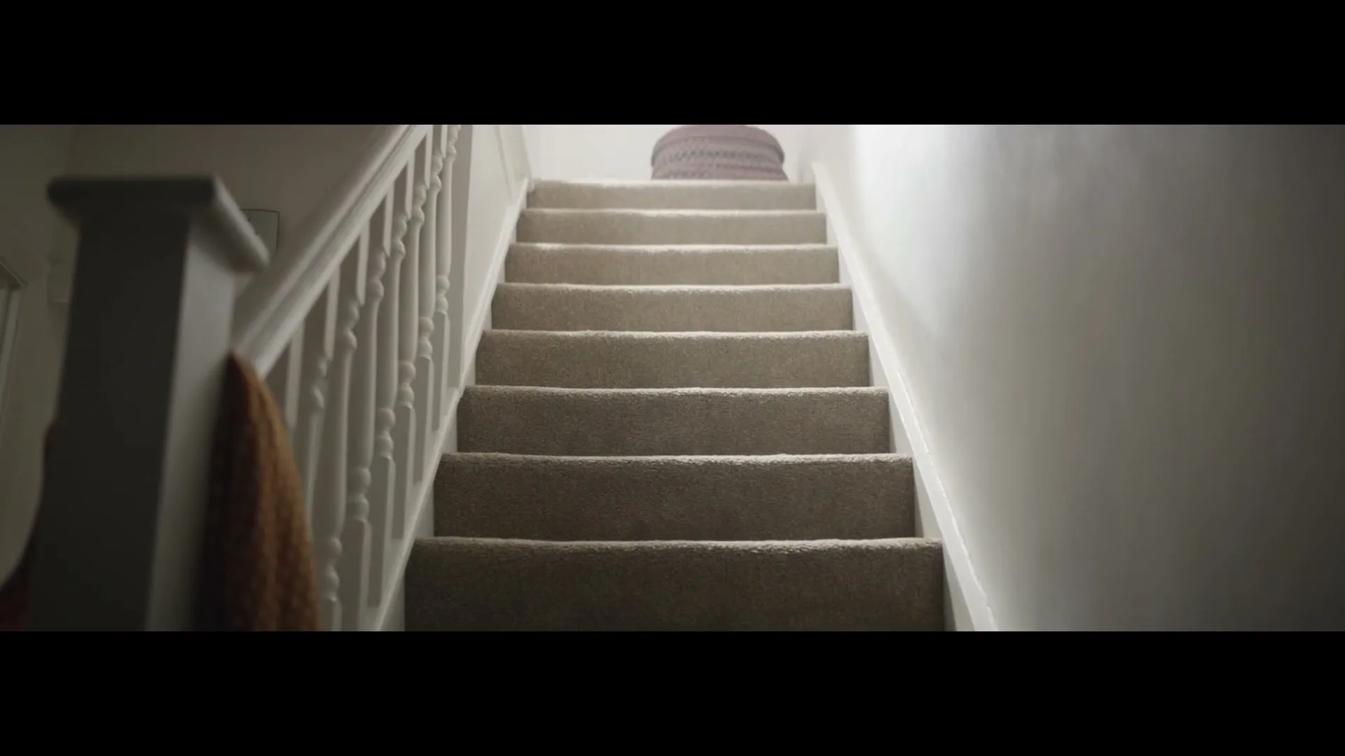 A carpeted staircase with white banisters leads upwards, with a glimpse of a woven basket at the top, in a dimly lit interior.
